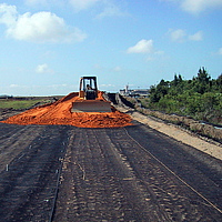 Bulldozer spreads sand over a laid Basetrac Grid geogrid for base course reinforcement on a construction site
