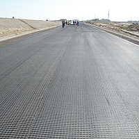 Laying of HaTelit grid on road surface before asphalting by construction workers.