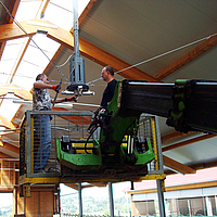 Two men repair the broken ceiling fan from a raised crane