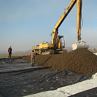 Excavator at work, spreading soil over the laid Basetrac® Woven reinforcement fabric