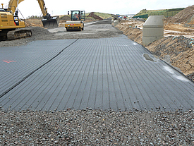Compaction of gravel surfacing on rolled-out Fortrac A geogrid with a roller for stable soil reinforcement
