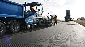 Tar machine lays asphalt on HaTelit XP reinforcement grid